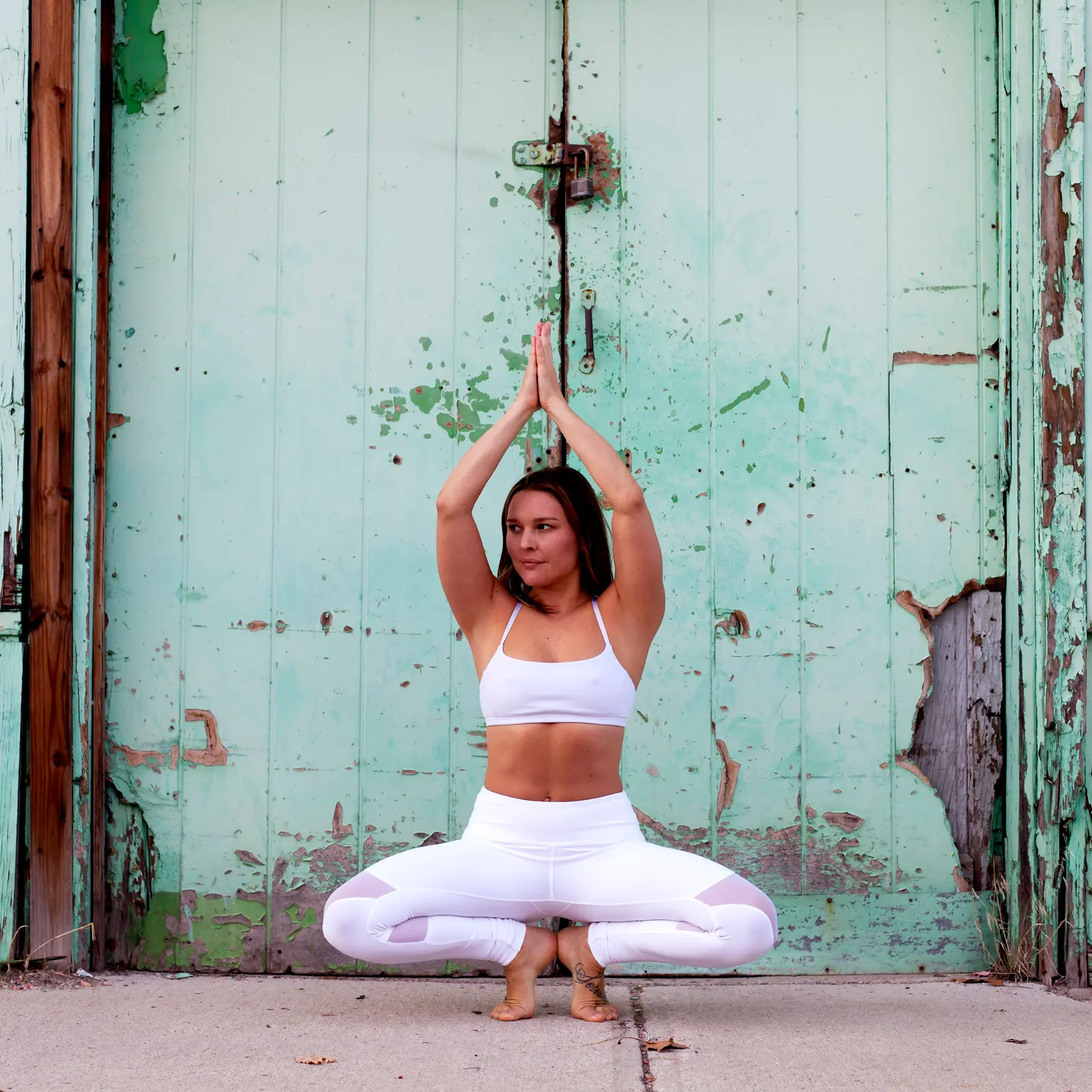 Michelle holding a centered yoga pose in front of a weathered green door