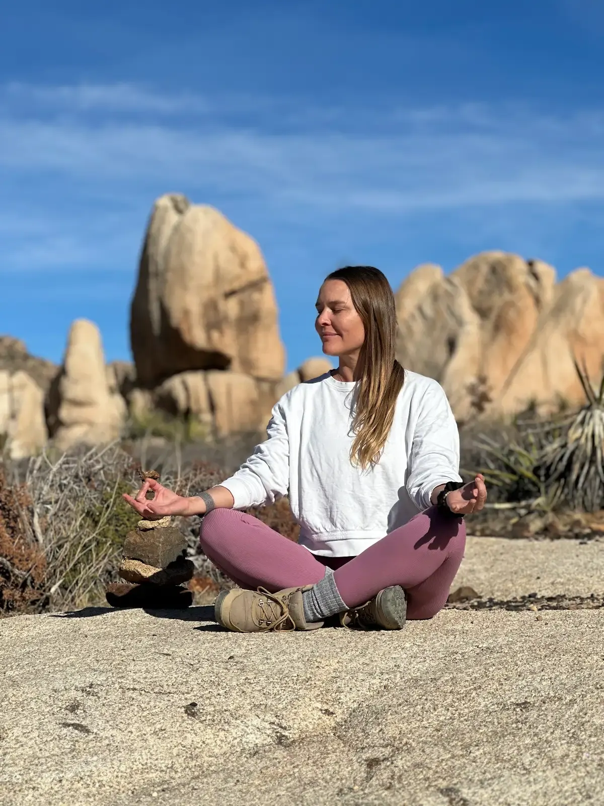Michelle seated in meditation on desert rock beneath a clear blue sky