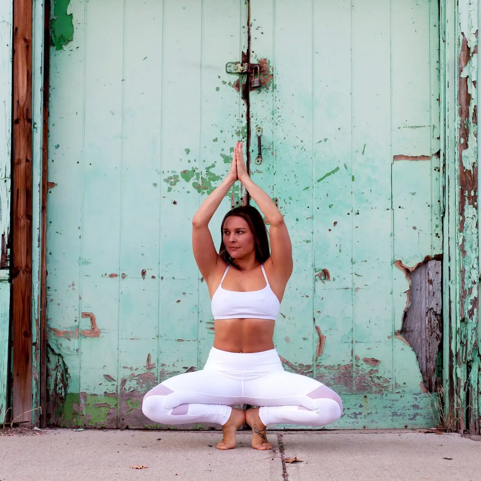 Michelle holding a centered yoga pose in front of a weathered green door